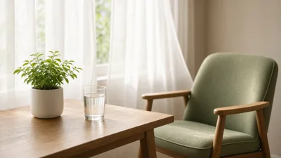 Soft morning light on a desk by a window with a plant, glass of water and an empty chair