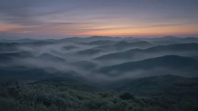 Evening mist drifting through layered hills after sunset