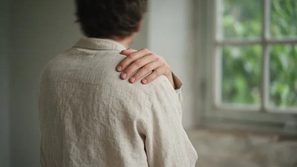 A hand gently kneading the top of the shoulder, seen from behind